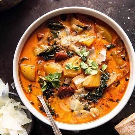 a bowl of soup with potatoes, spinach and other vegetables in it on a table