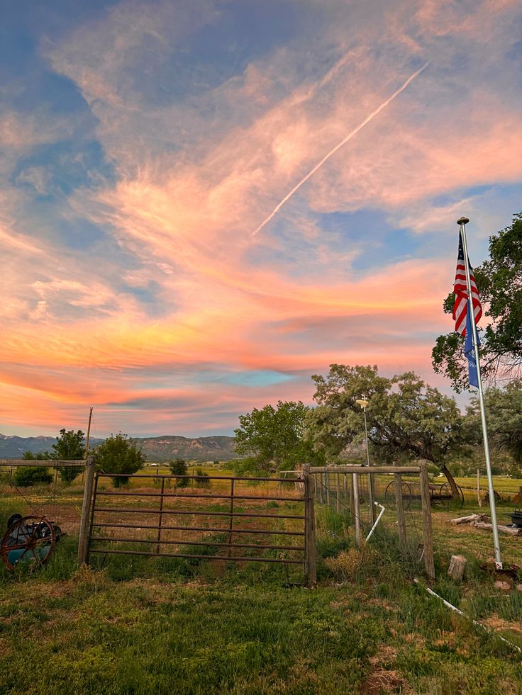 an american flag flying in the sky over a fenced in area with trees and grass