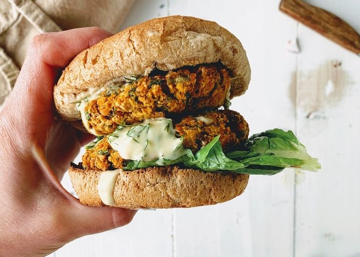 a hand holding a sandwich with lettuce and sauce on it, next to cinnamon sticks