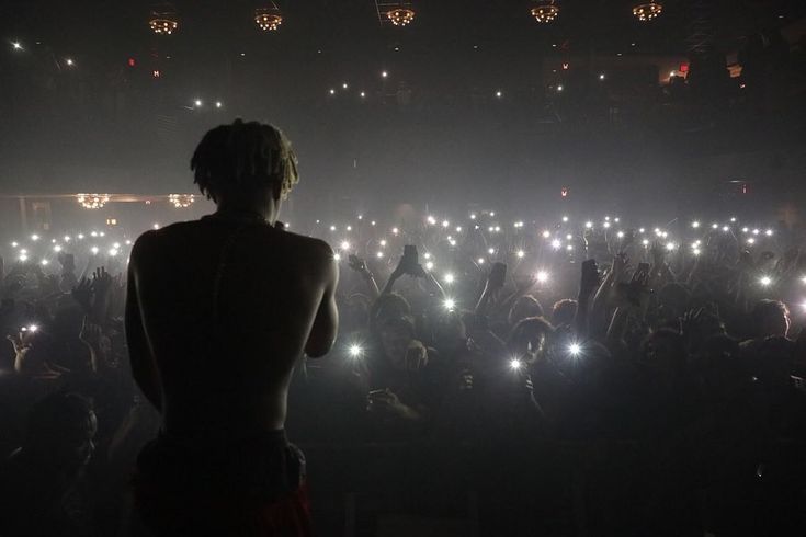 a woman standing in front of a crowd holding up her cell phone at night time