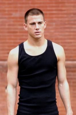 a man in black shirt and shorts holding a frisbee near brick wall with bricks behind him