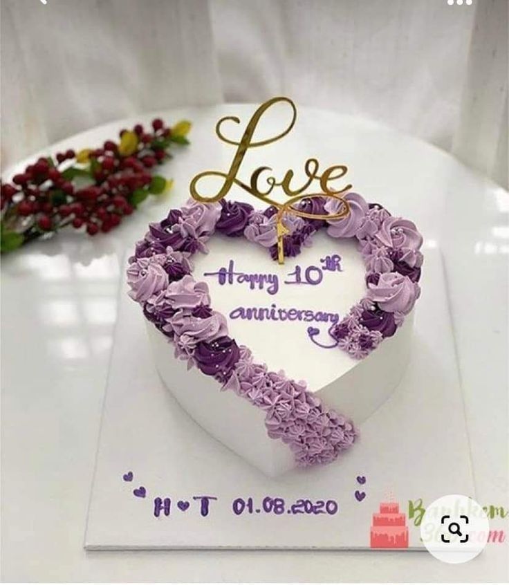 a white heart shaped cake with purple flowers on it and the word love written in gold