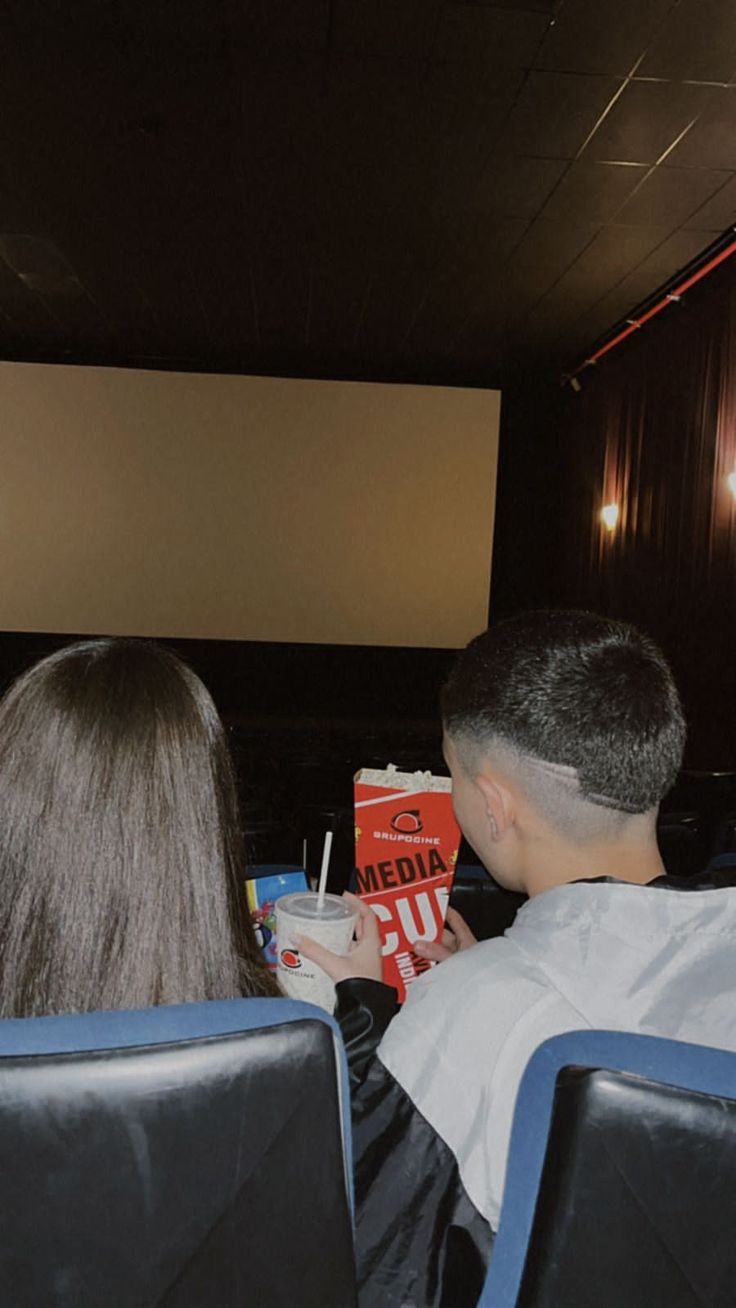 two people sitting in chairs looking at a movie on the wall behind them is a projector screen