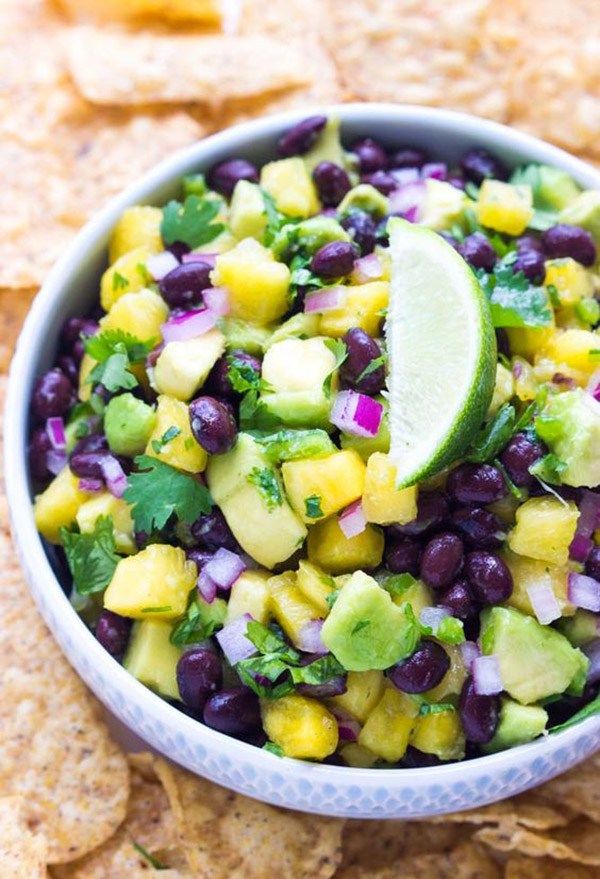 a white bowl filled with black beans, avocado and pineapple salsa surrounded by tortilla chips