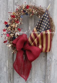 a patriotic wreath with an american flag on it hanging on a wooden fence, decorated with red, white and blue stars