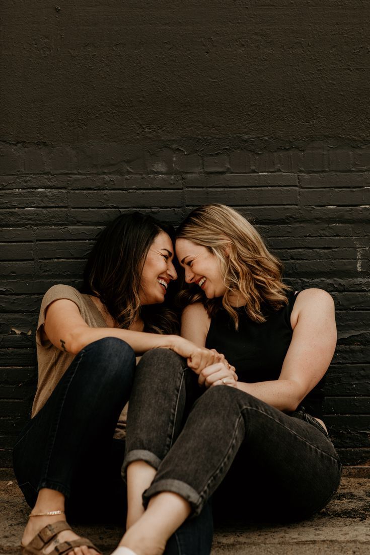 two women sitting next to each other on the ground hugging and smiling at each other