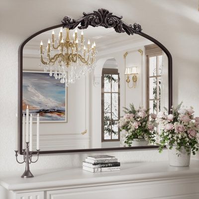 a mirror that is sitting on top of a mantle next to a vase with flowers