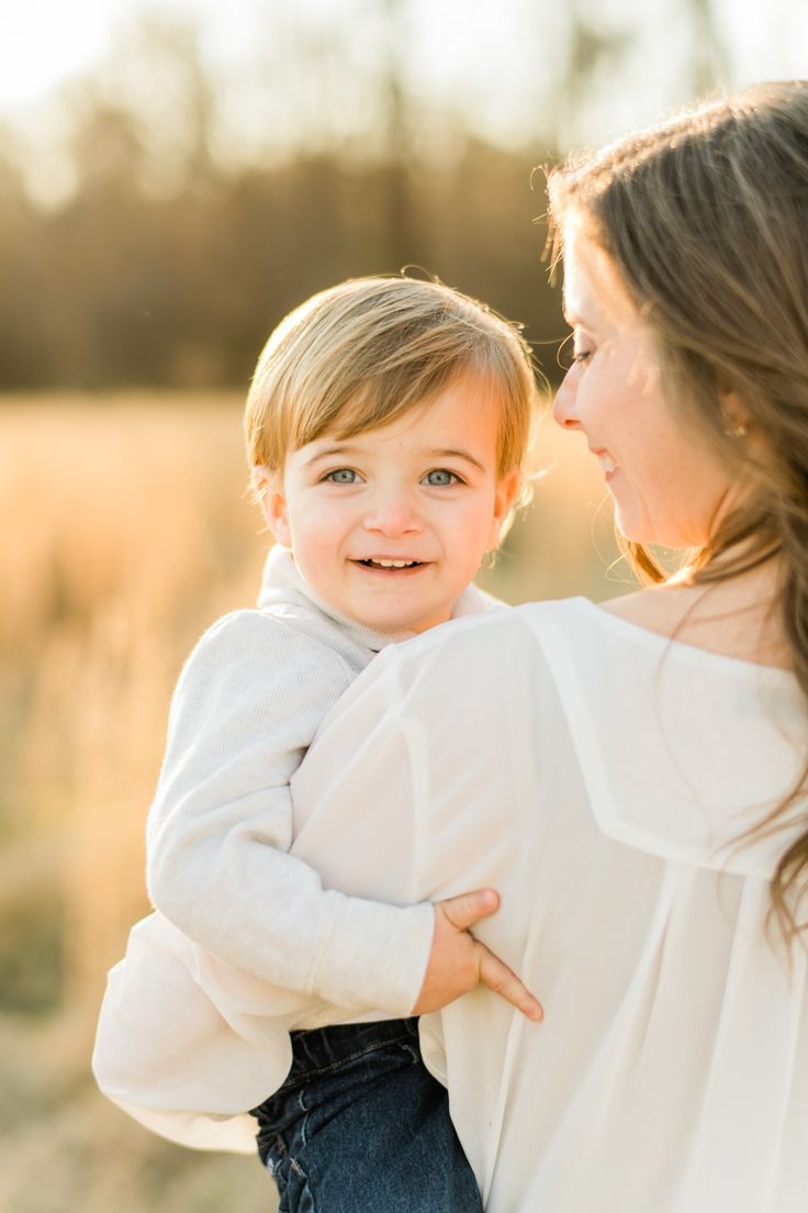 a woman holding a child in her arms and smiling at each other with the sun shining on them