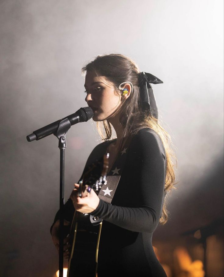 a woman singing into a microphone while holding a guitar in her right hand and wearing headphones