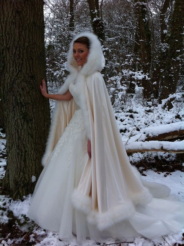 a woman in a wedding dress standing next to a tree wearing a white fur stole