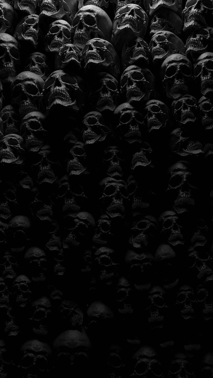 black and white photograph of many skulls in the dark, with only one head visible