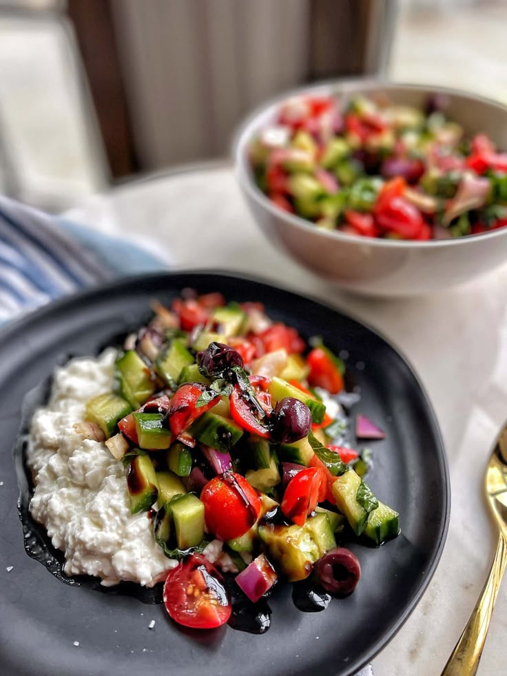 a black plate topped with mashed potatoes and veggies next to a bowl of salad