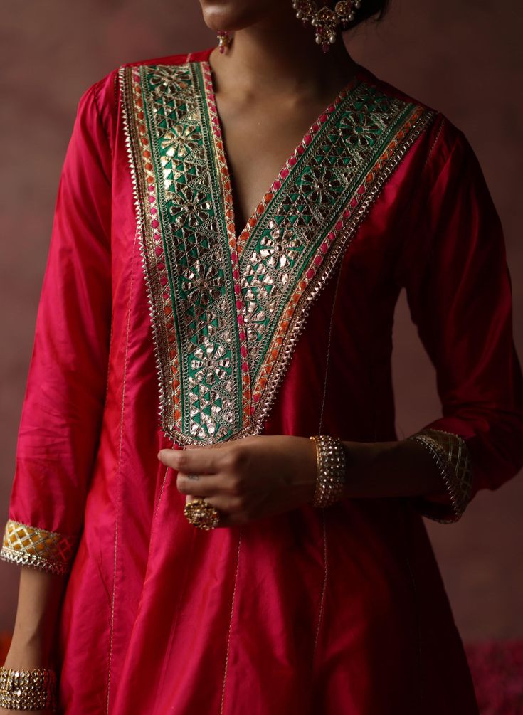 The short A-line kurta in silk makes a pop with the contrast gota patti work on the neck and sleeves. The set is complemented by pants adorned with silk brocades and zari embroidery and a contrasting organza dupatta with golden-colored fringed lace. Luxury Zari Work Tissue Silk Kurta, Luxury Raw Silk Unstitched Suit With Zari Work, Luxury Unstitched Raw Silk Suit With Zari Work, Luxury Slub Silk Kurta With Embroidered Border, Luxury Banarasi Silk Salwar Kameez With Dori Work, Luxury Straight Kurta With Embroidered Neckline, Luxury Multicolor Embroidered Kurta For Festive Occasions, Luxury Festive Kurta With Motifs, Luxury Pista Green Kurta With Gota Work