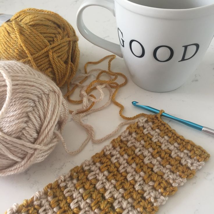 two balls of yarn next to a crochet mug cozying mat and a cup of coffee