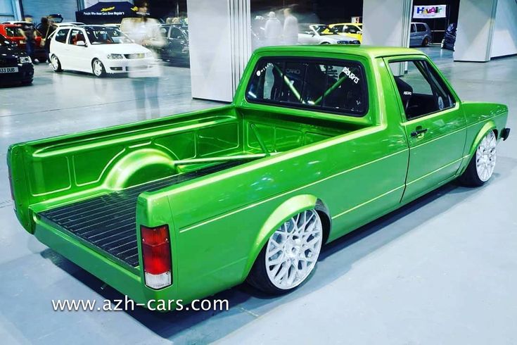 a green pick up truck is parked in a showroom with other cars behind it