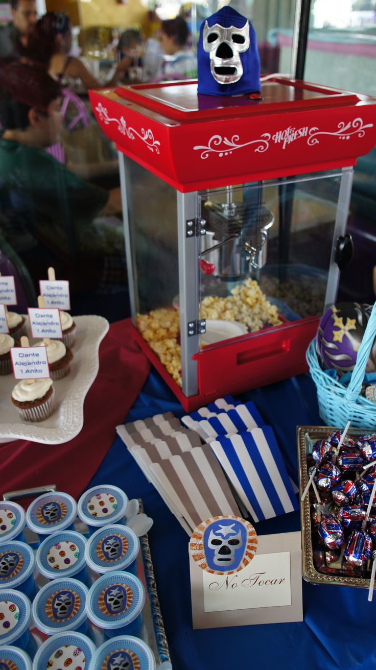 a table topped with lots of cupcakes and candy covered desserts next to a popcorn machine