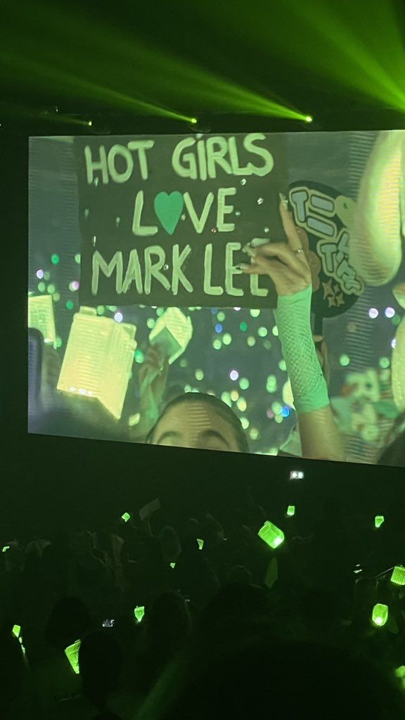 a person holding up a sign in front of a crowd at a concert with green lights