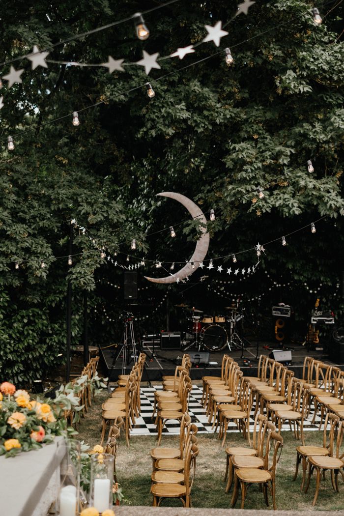 an outdoor event with wooden chairs and string lights strung from the trees, stars and moon decorations