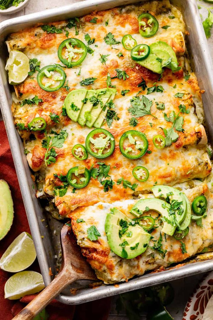 an enchilada casserole in a baking pan with sliced avocado on the side