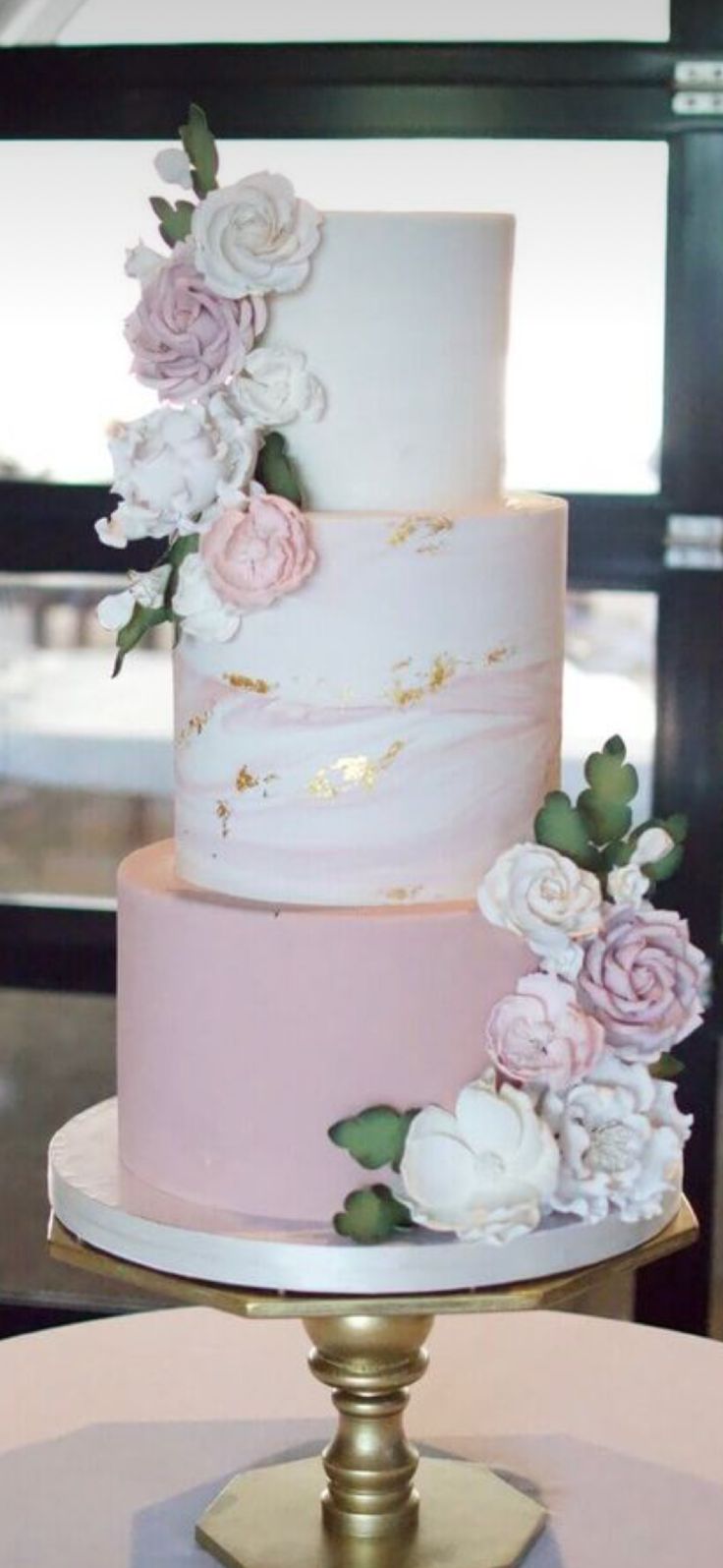 a three tiered cake with pink and white flowers on the top is sitting on a gold plate