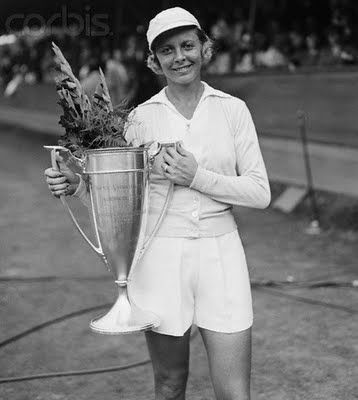 an old black and white photo of a tennis player holding a trophy in her hands