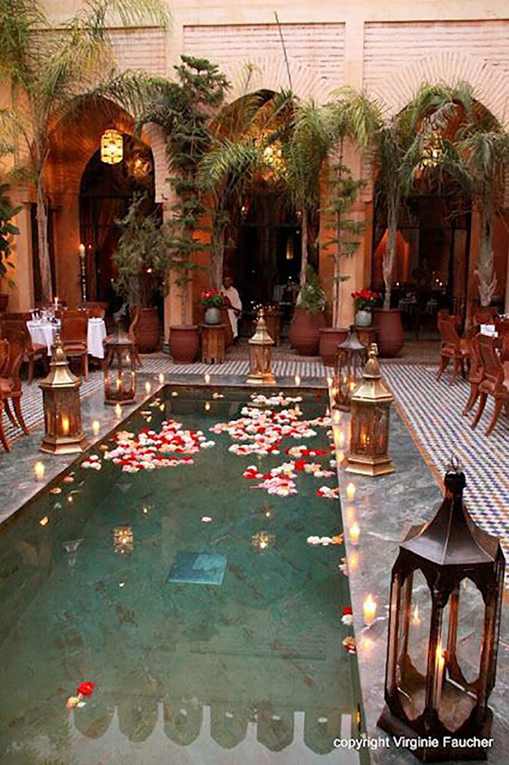 a pool surrounded by tables and chairs with candles on them in the middle of a courtyard