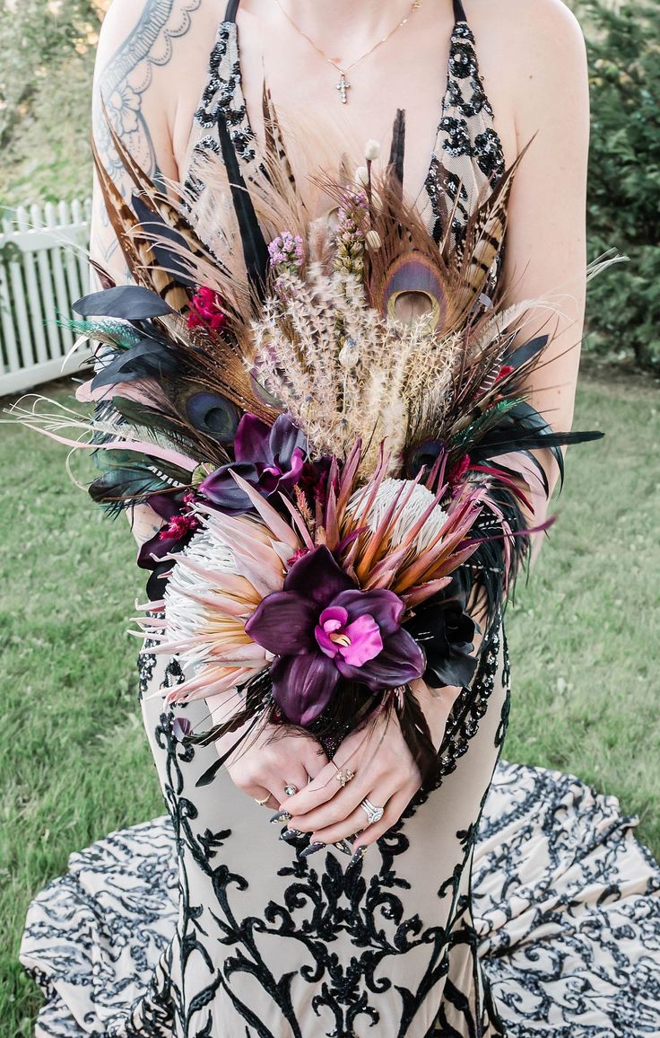 a woman wearing a dress with feathers and flowers in her hair is holding a bouquet