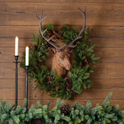 a deer head mounted to the side of a wooden wall next to pine cones and candles