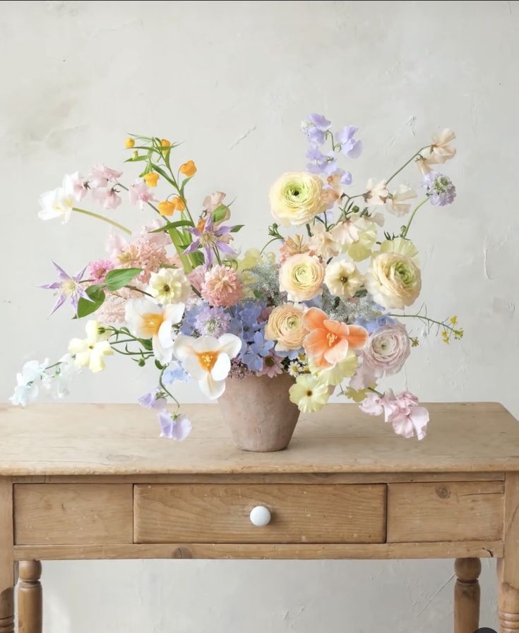 a wooden table topped with a vase filled with lots of different colored flowers on top of it