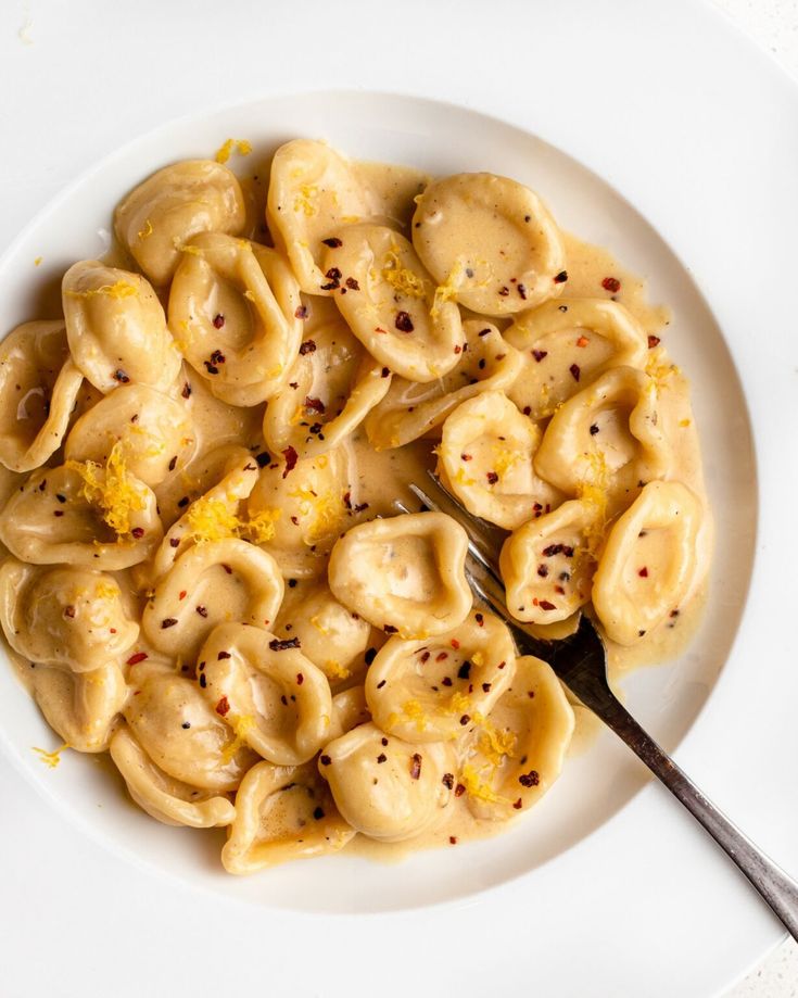 a white plate topped with pasta covered in sauce and garnished with seasoning