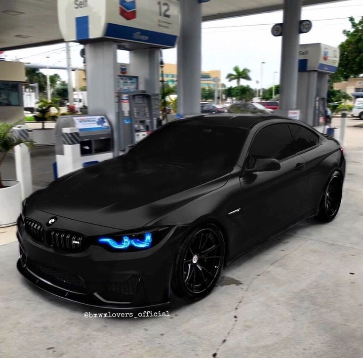 a black car parked in front of a gas station with blue lights on it's hood