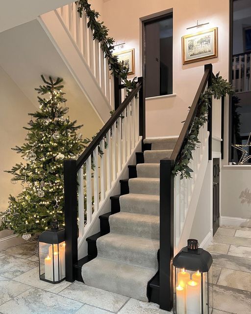 two lit candles sitting on the steps next to a christmas tree and stairs leading up