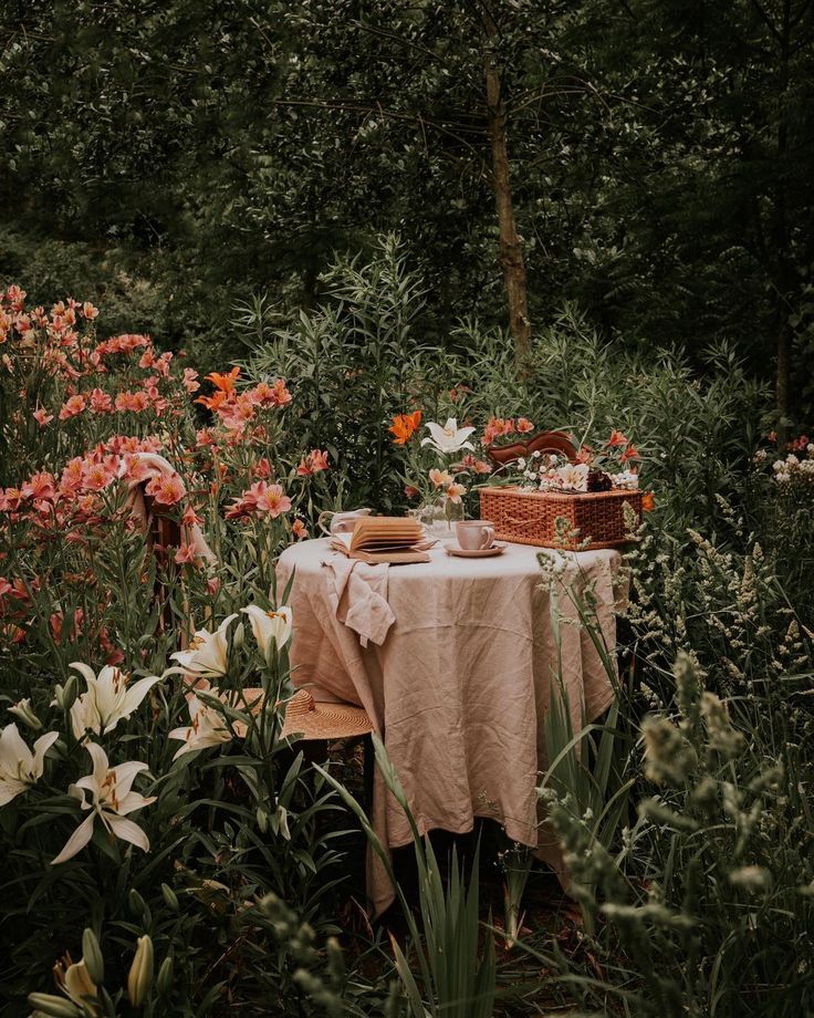 a picnic table in the middle of a field with flowers around it and a basket full of food on top