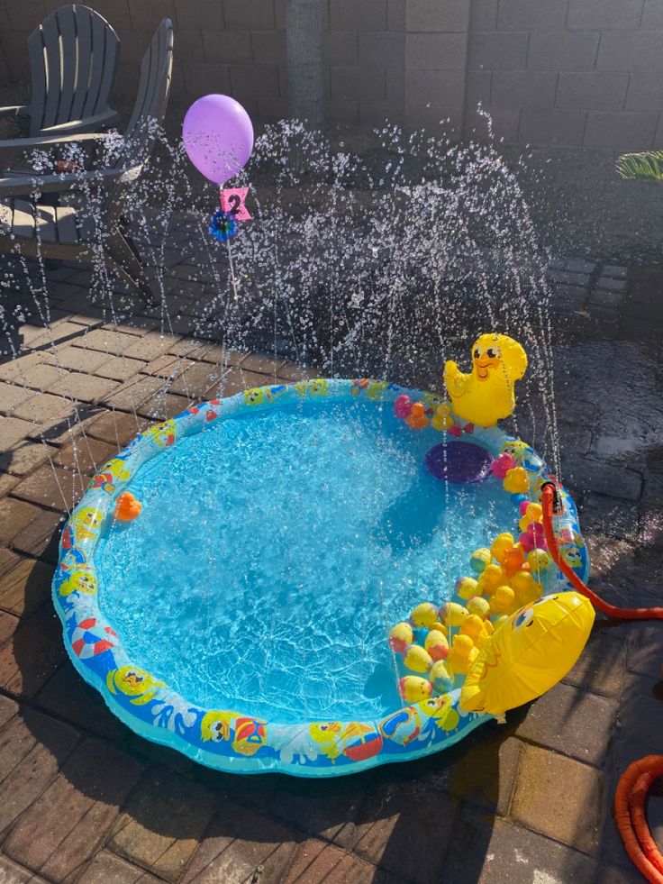 an inflatable swimming pool with water spouting from it and rubber ducks floating around