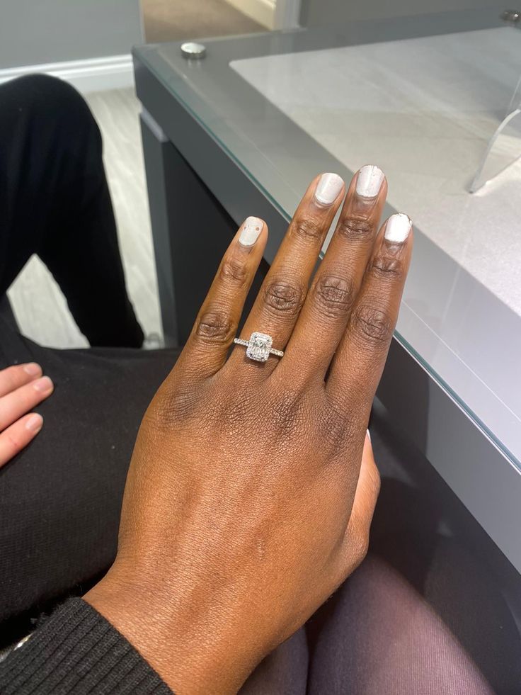 a woman's hand with a diamond ring on her left hand, sitting in front of a glass display case