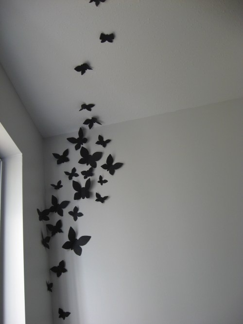 a flock of black butterflies flying in the air over a white wall and window sill