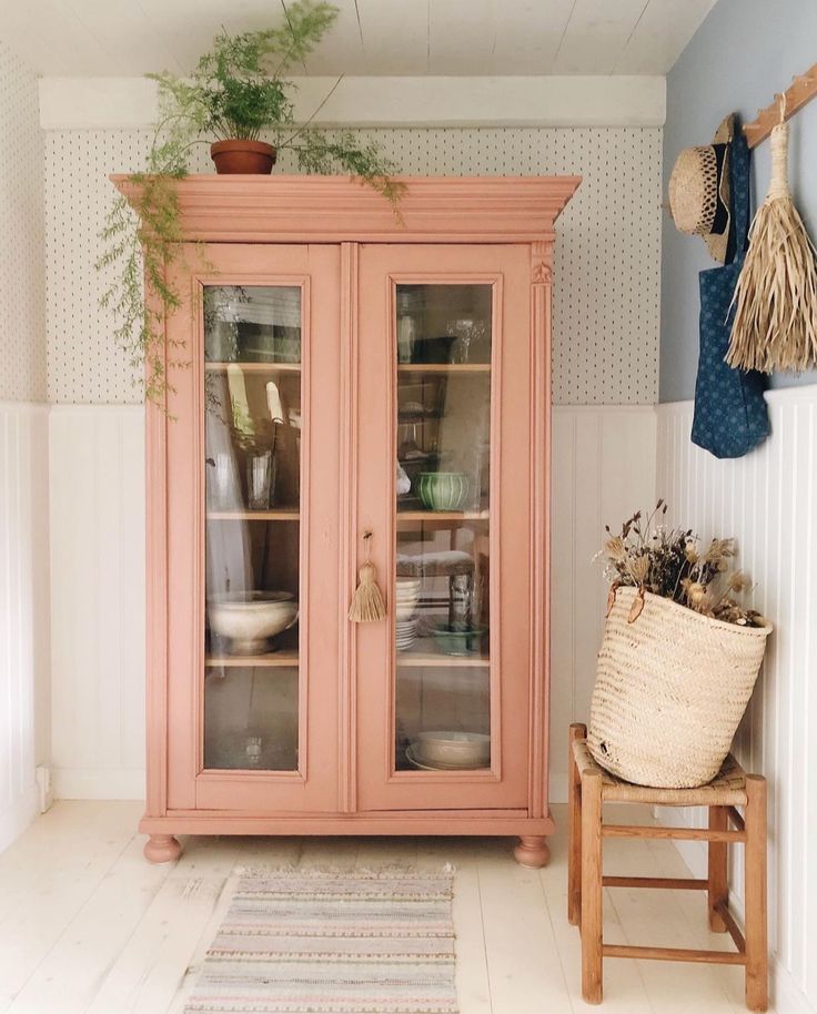 a pink china cabinet with glass doors and plants on the top shelf next to it