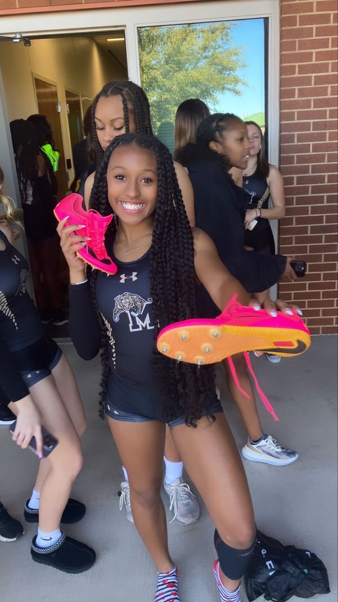 two girls are holding up pink objects in front of a brick building while another girl is standing next to them