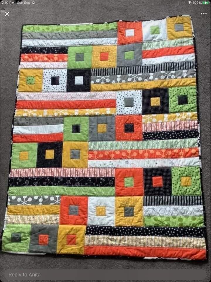 a colorful quilt is on the floor in front of a black tablecloth with an orange, yellow and green patchwork design