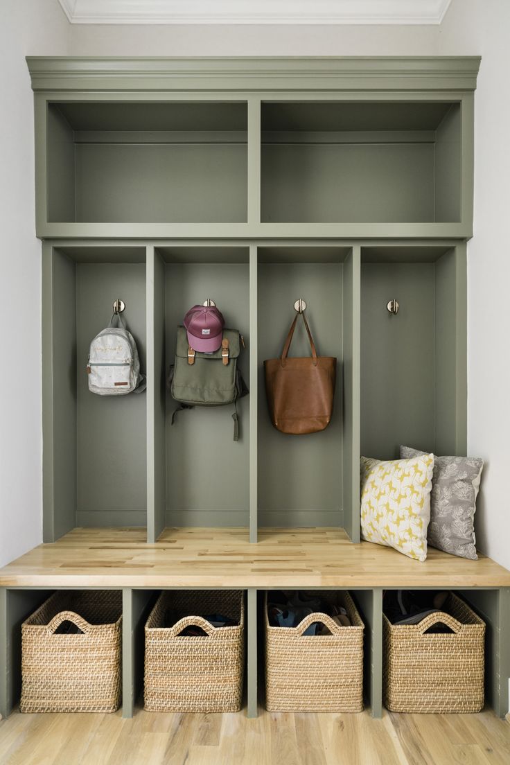 a bench with baskets and purses on it in front of a wall mounted coat rack