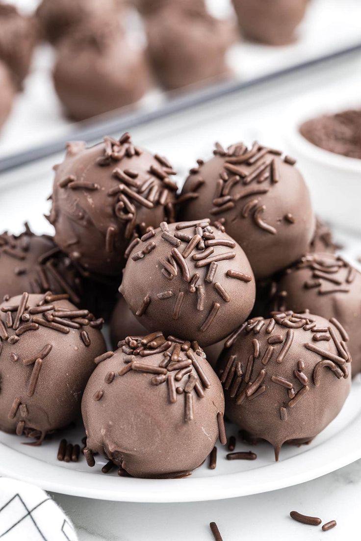 chocolate truffles with sprinkles on a white plate next to other dessert items