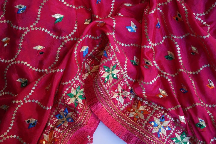 Phulkari refers to the folk embroidery of the Punjab. Although phulkari means floral work, the design include not only flowers but also covers motifs and geometrical shapes. The craft of phulkari has undergone changes over the centuries. This gorgeous colorful phulkari on pure chinnon in hot pink color is so versatile and can be worn as a dupata, scarf or on any wedding occasion. Our phulkaris are handcrafted to perfection keeping in mind the authenticity of the culture in an urban way. Stand ou Traditional Multicolor Embroidered Wear For Puja, Traditional Wear With Multicolor Embroidery For Puja, Pink Embroidered Fabric With Motifs For Navratri, Navratri Pink Embroidered Fabric With Motifs, Traditional Red Dupatta With Mirror Work, Festive Jamawar Embroidered Fabric For Navratri, Navratri Jamawar Embroidered Fabric With Motifs, Traditional Embroidered Fabric For Diwali, Festive Multicolor Embroidered Chanderi Fabric