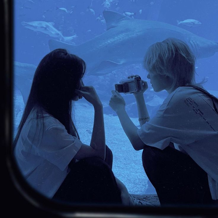 two people are looking at a shark in an aquarium while the woman is holding a camera