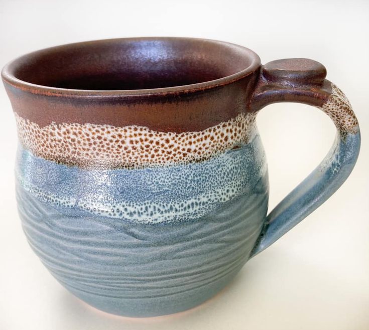 a blue and brown ceramic mug with wavy lines on the outside, sitting on a white surface