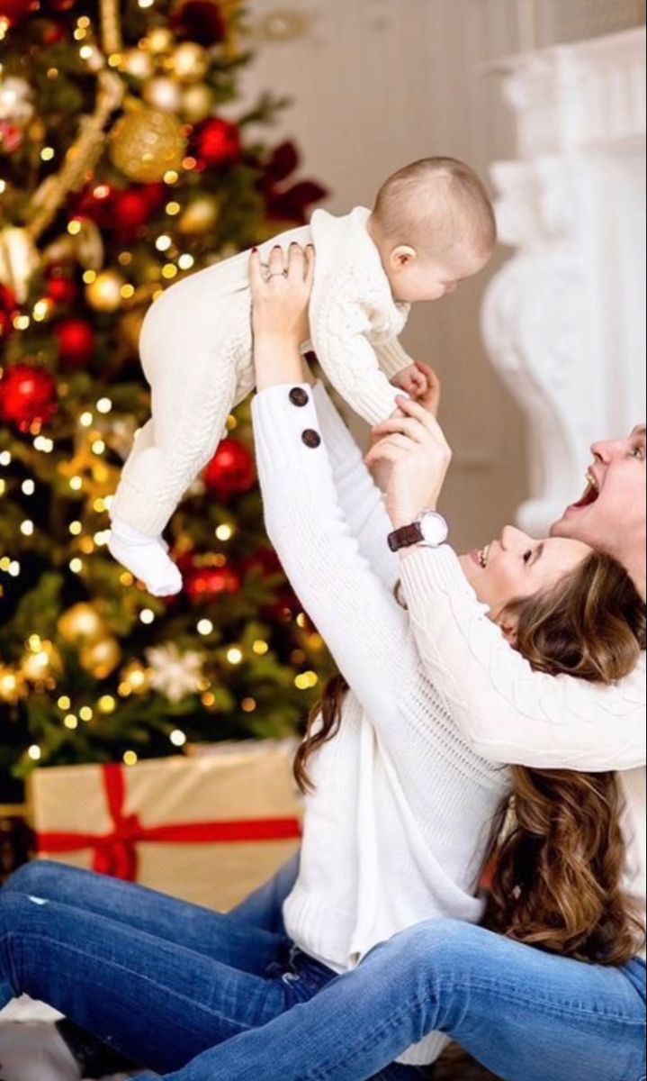 a man and woman holding a baby in front of a christmas tree