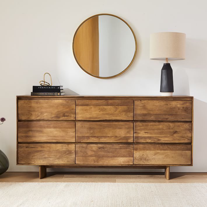 a wooden dresser sitting next to a round mirror on top of a white wall in a living room