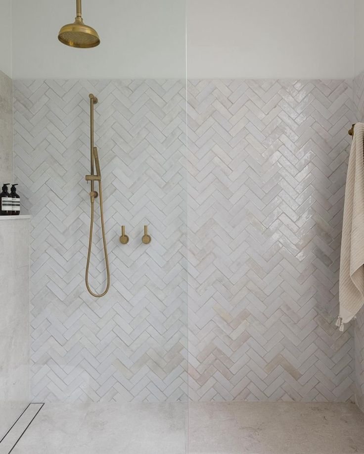 a bathroom with white tile and gold shower faucet next to a walk in shower