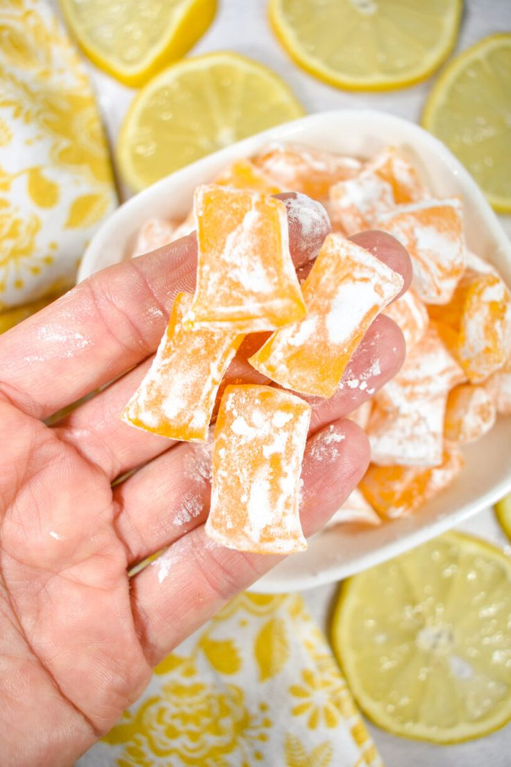 a hand holding a small bowl filled with orange and lemon squares