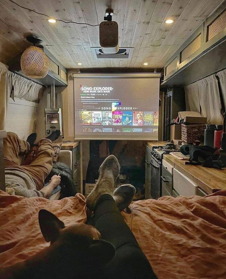 two people and a dog in a camper with a projector screen on the wall