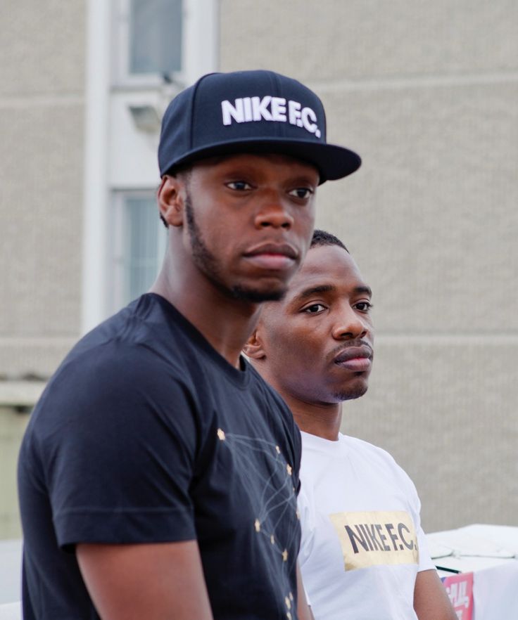 two men standing next to each other in front of a building with a nike hat on